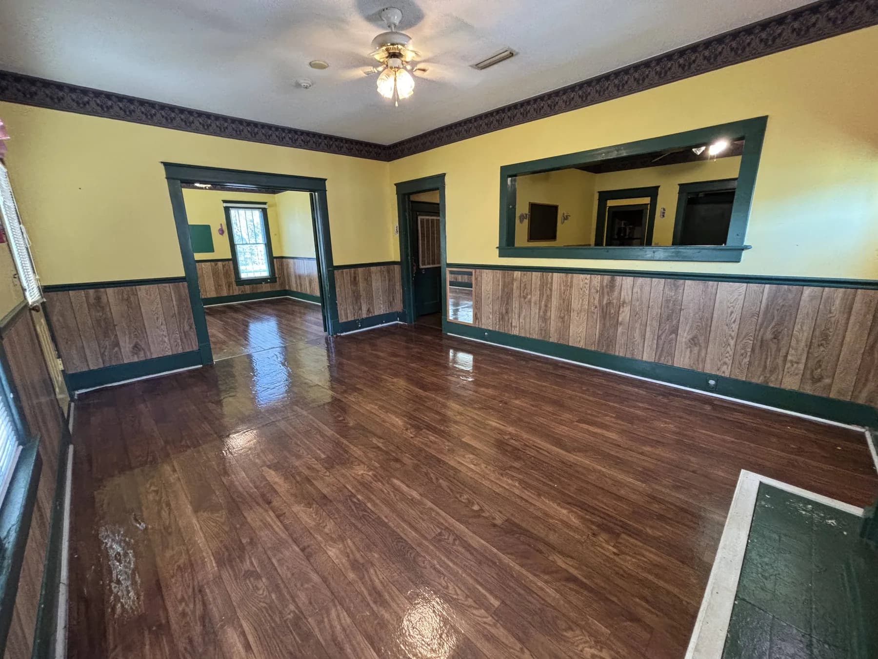 Empty front room with wood floors, green trim, yellow walls, and a large interior opening.